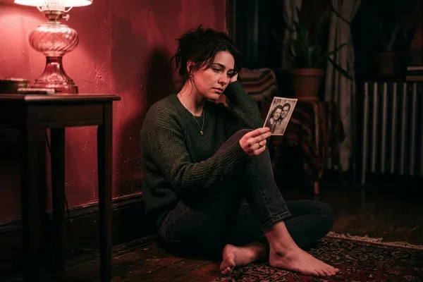 女人坐在牆邊凝視手中照片，神情複雜又清醒